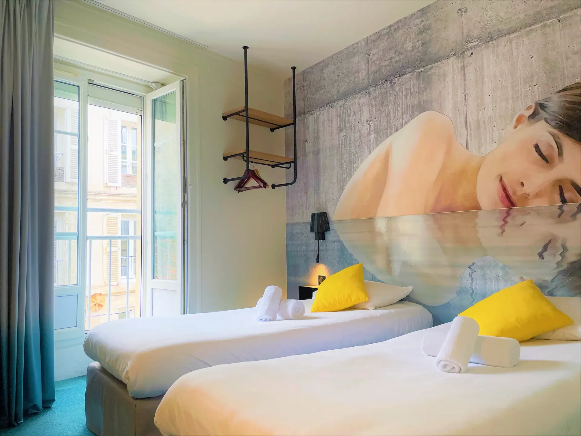 Chambre twin de l'hôtel Le Bord'O : deux lits simples, oreillers jaunes et fresque murale d'un visage de femme